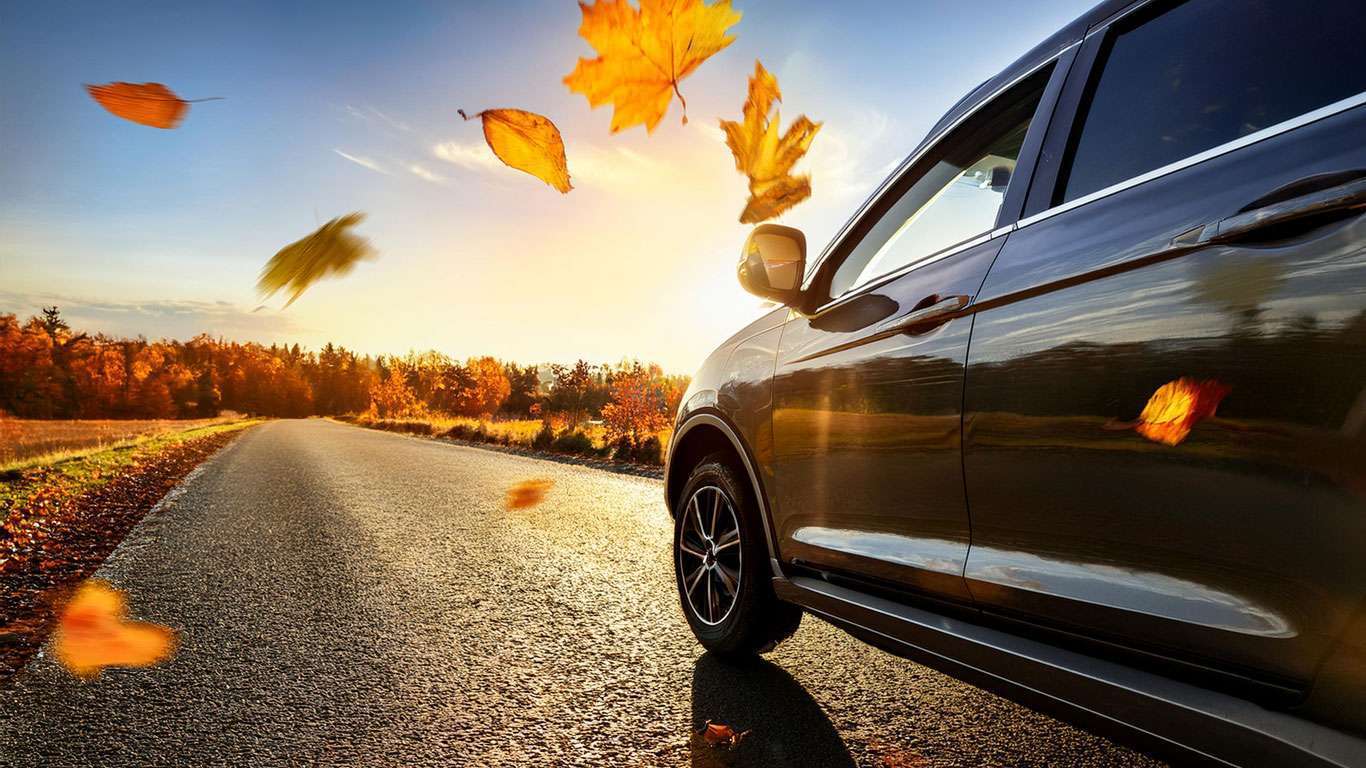 Imagen frontolateral de un coche en la carretera y hojas movidas por el viento