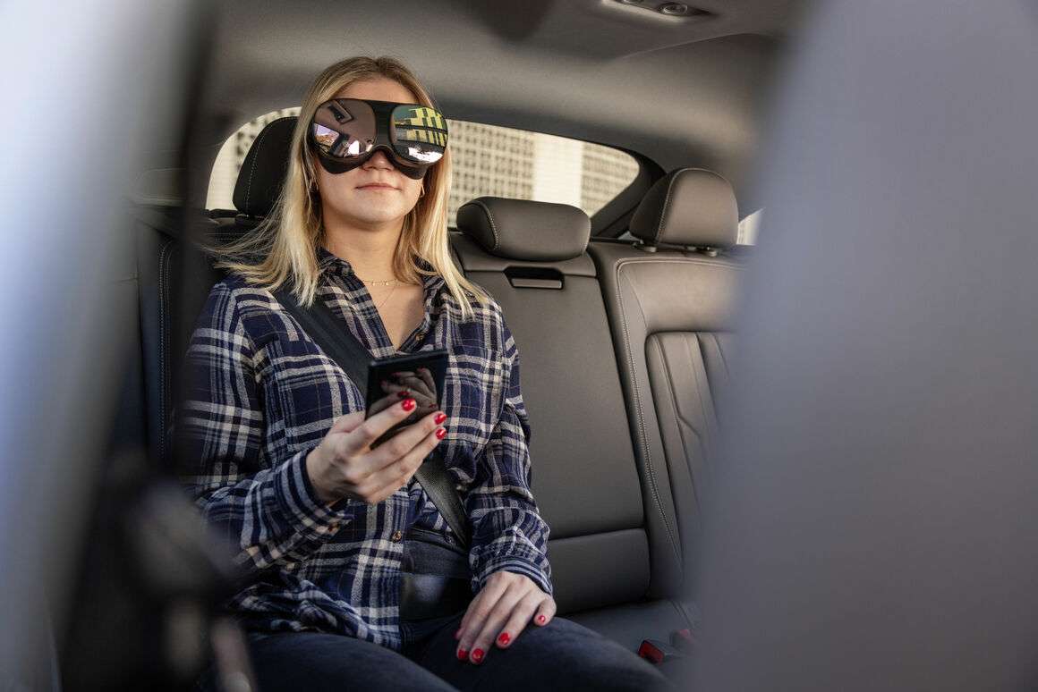 Mujer en asiento trasero de auto con gafas de sol y teléfono en mano