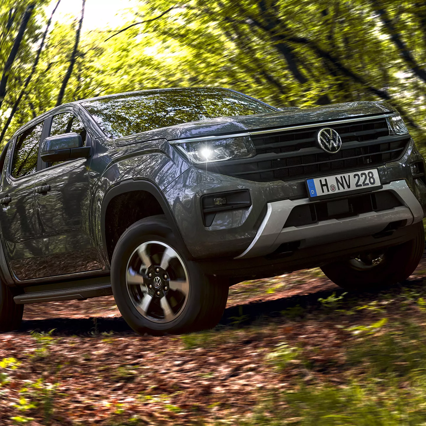 Volkswagen Amarok gris oscuro atravesando un sendero boscoso con hojas verdes a su alrededor