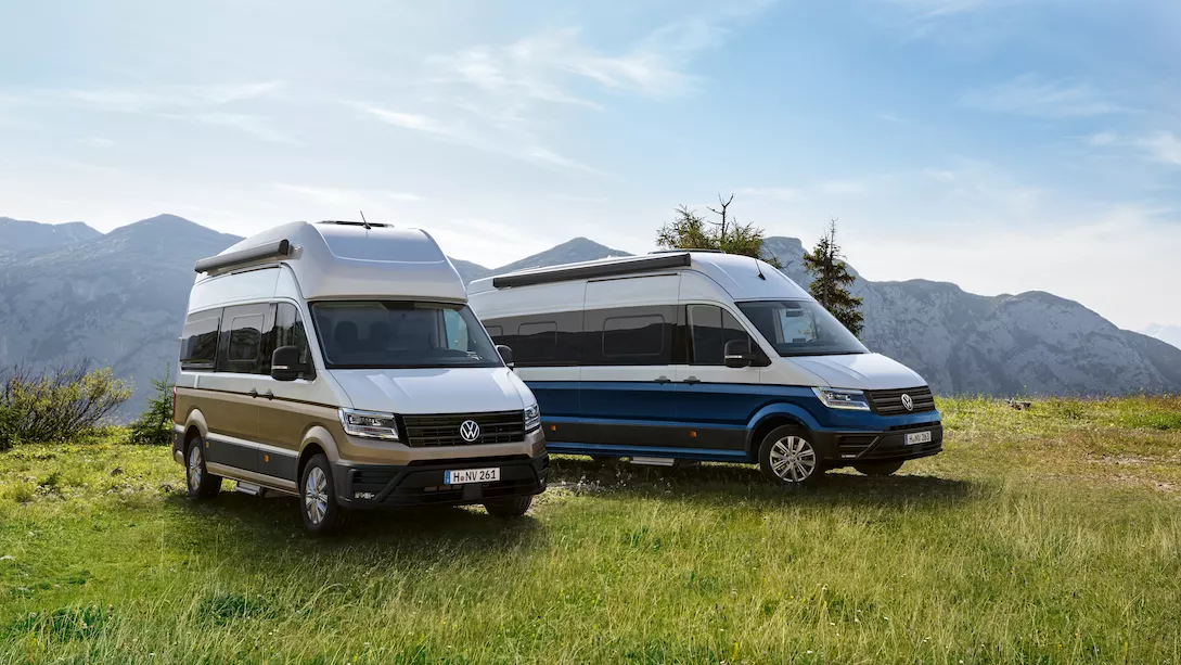 Dos Volkswagen Gran California aparcados en un campo verde con montañas al fondo, en un entorno natural.