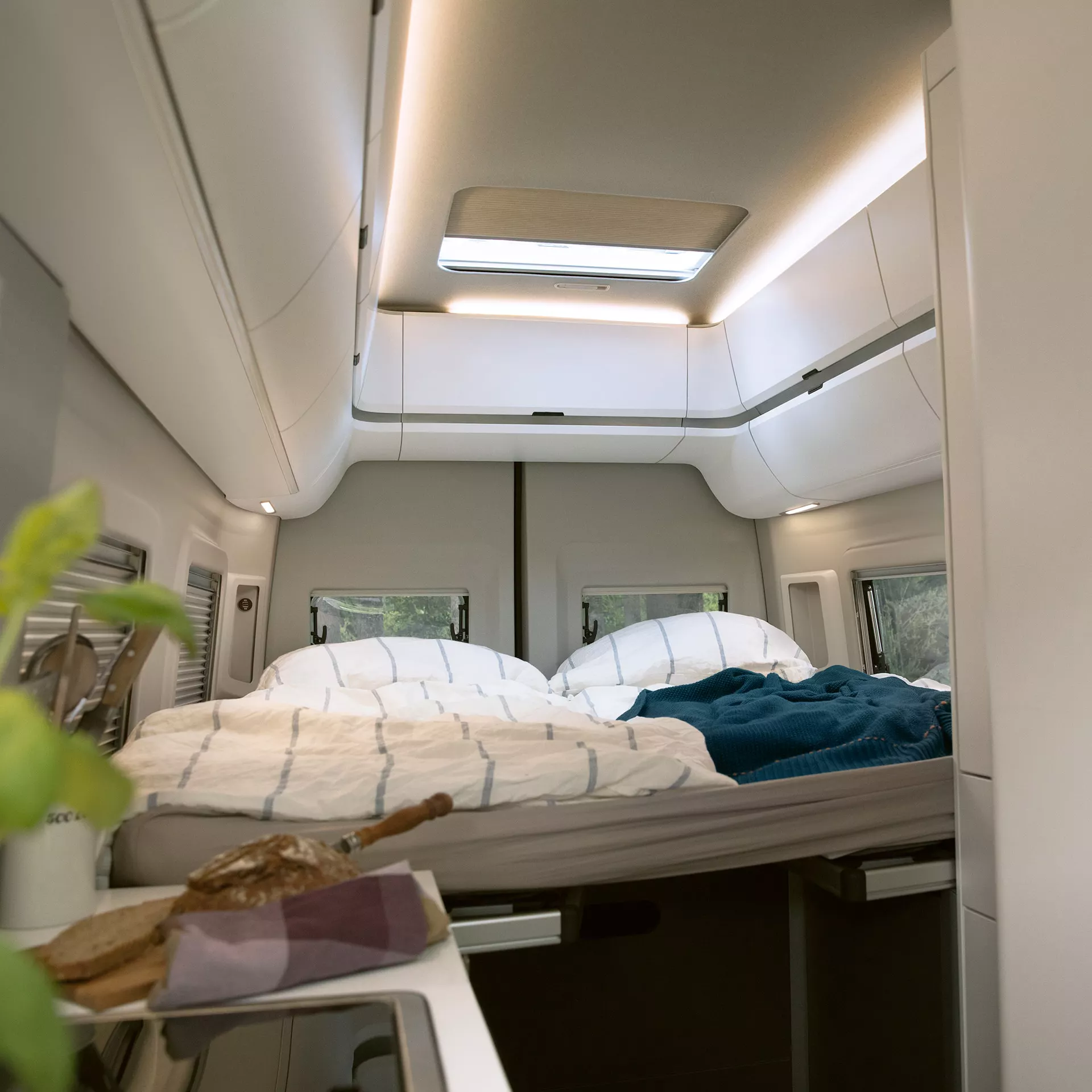 Interior de una autocaravana Volkswagen Gran California con dos camas plegables, iluminación integrada y espacio de almacenamiento.