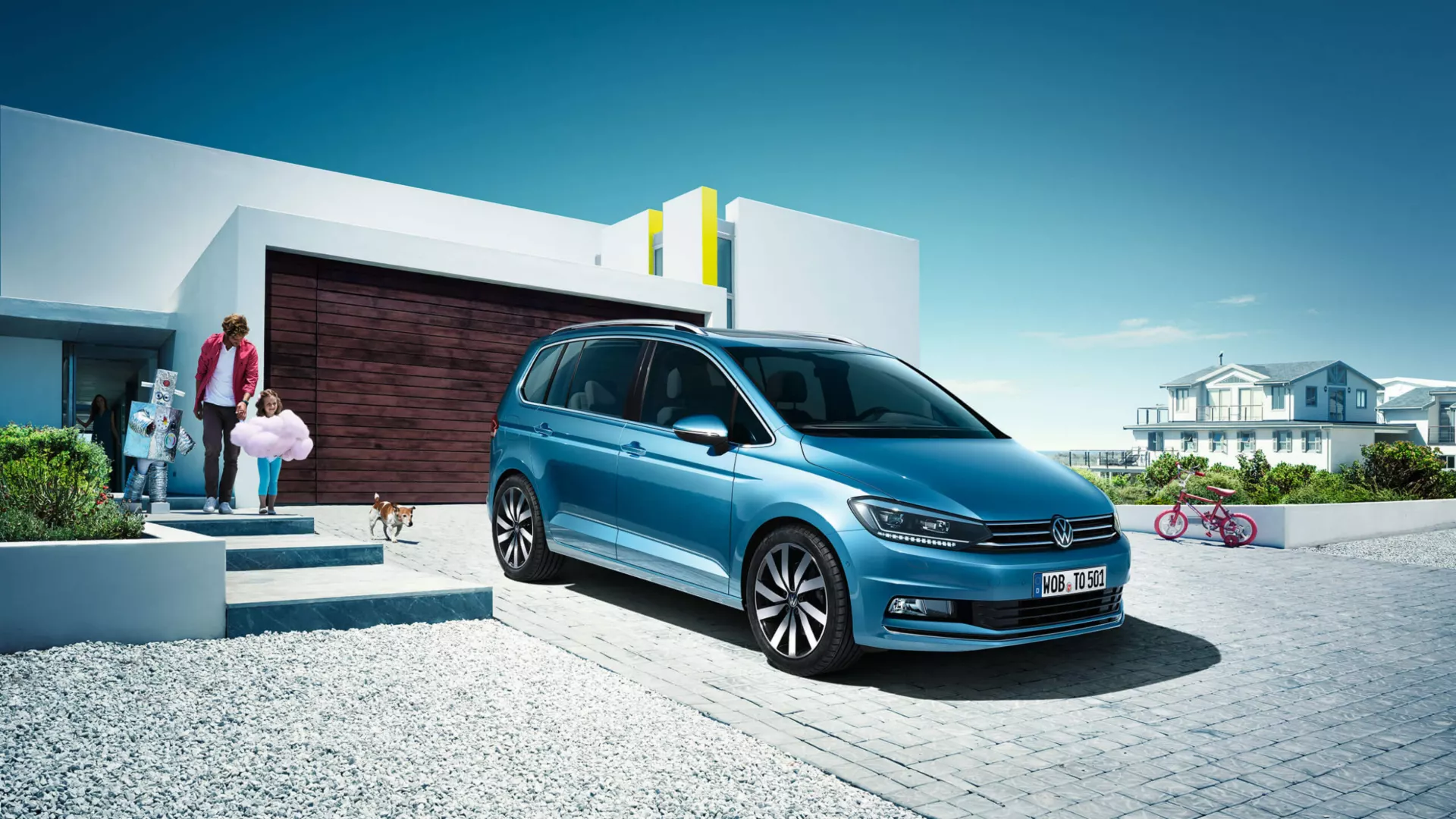 Familia saliendo de una casa moderna con un automóvil Volkswagen Touran azul estacionado en el frente