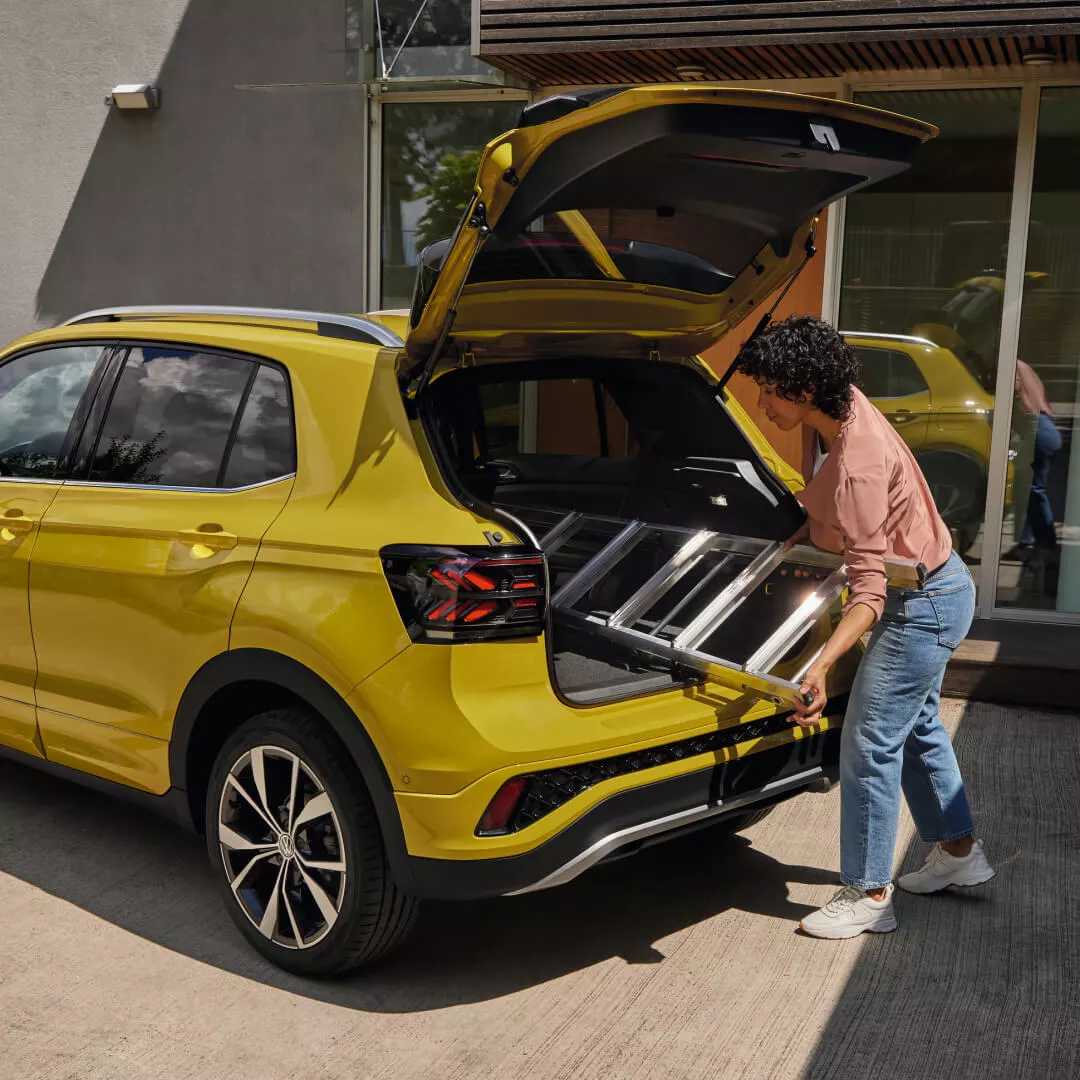 Persona cargando el maletero de un coche Volkswagen amarillo, con el portón trasero abierto y el interior del vehículo a la vista.
