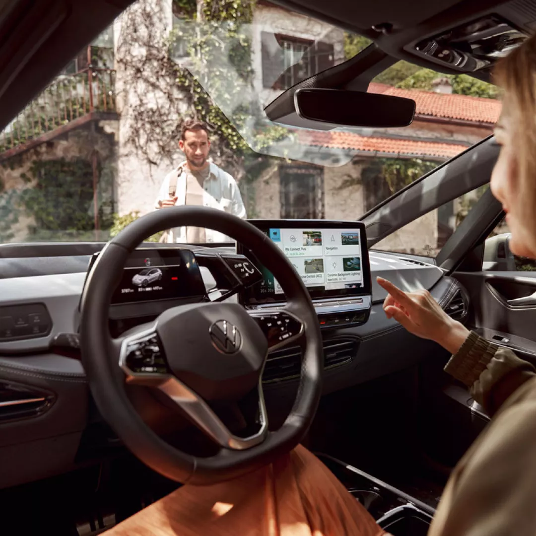 Interior de un vehículo Volkswagen ID.3 con un panel de control central que muestra información de viaje y navegación, mientras el conductor interactúa con el sistema de infotainment.