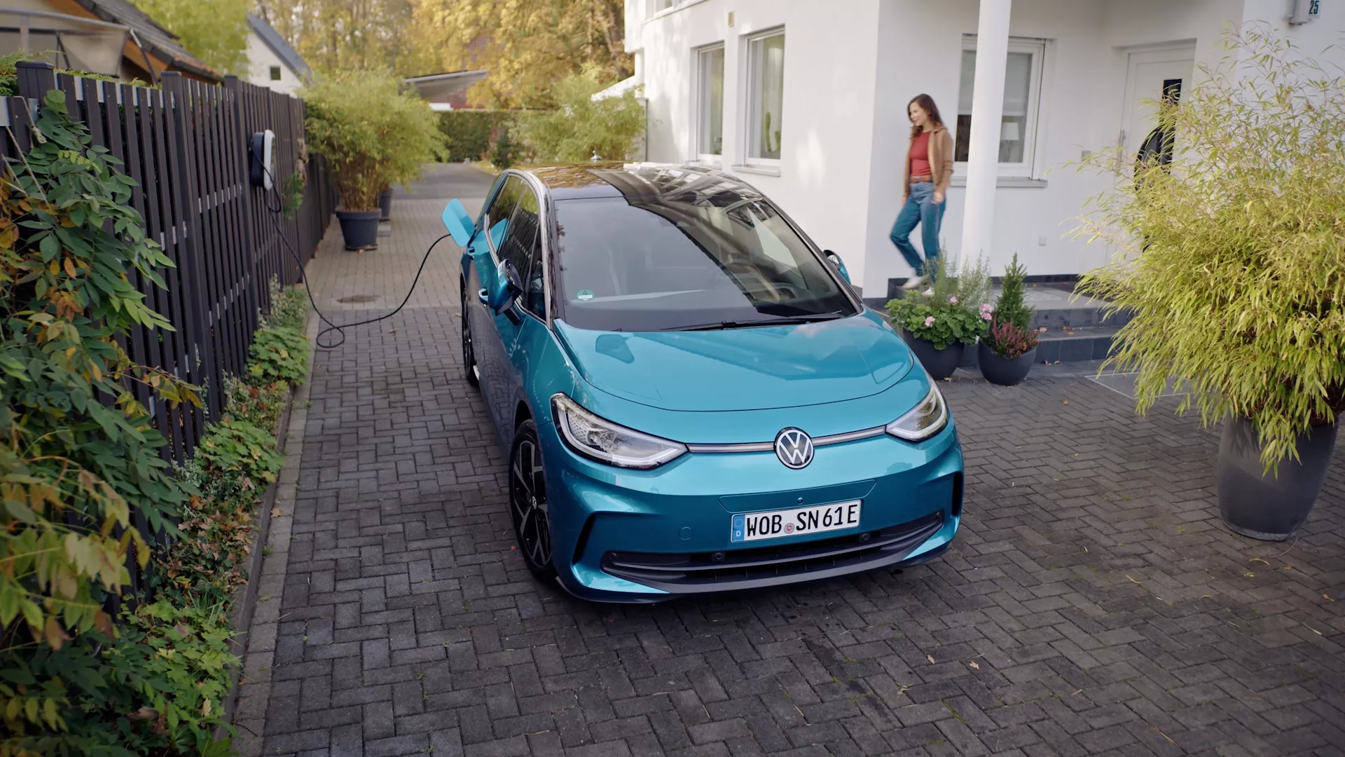 Volkswagen ID.3, un vehículo eléctrico de color turquesa, cargándose en un camino de adoquines junto a una casa con vegetación alrededor