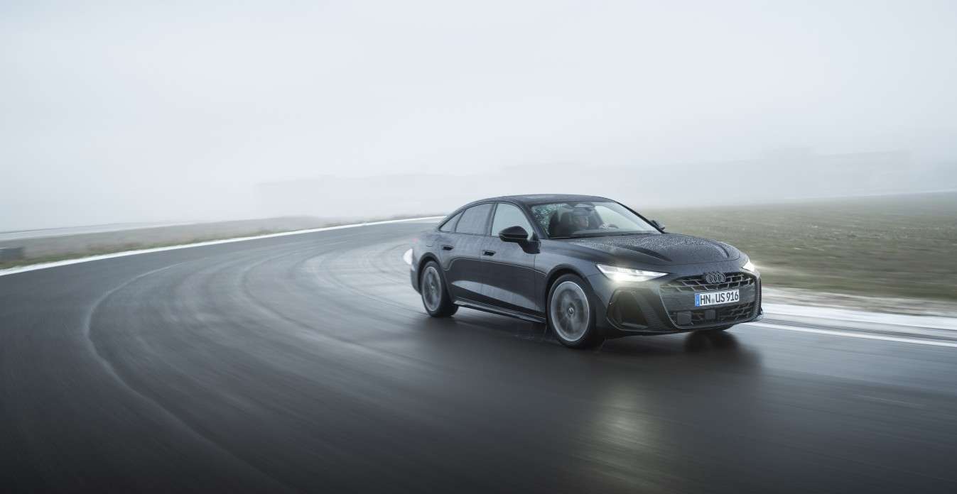 Un automóvil Audi deportivo de color oscuro conduciendo a alta velocidad por una carretera con niebla en el fondo