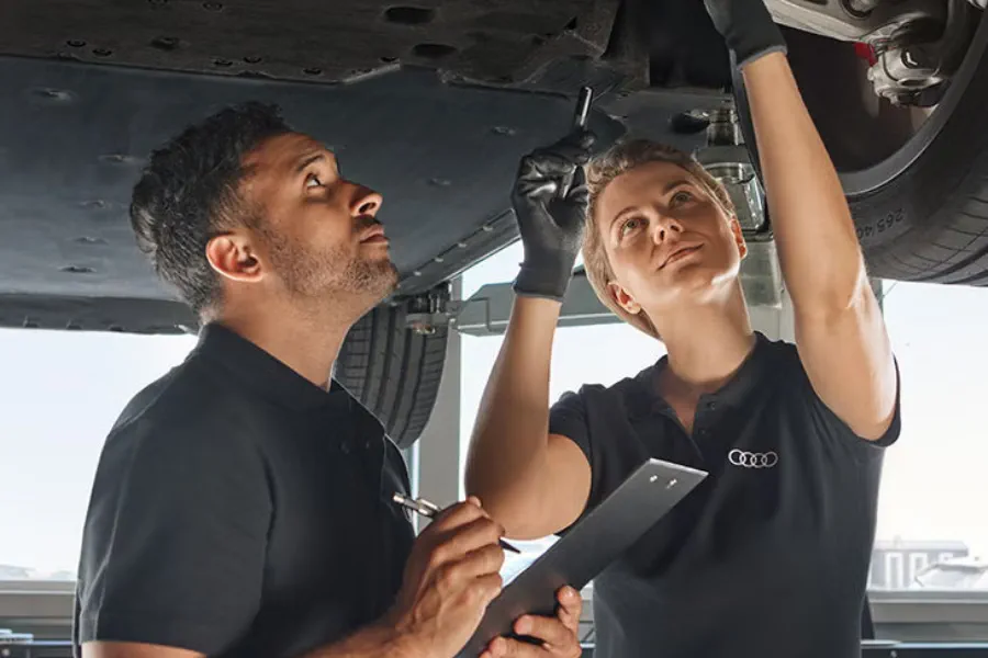 Dos técnicos de Audi revisan un vehículo con una tablet bajo el capó.