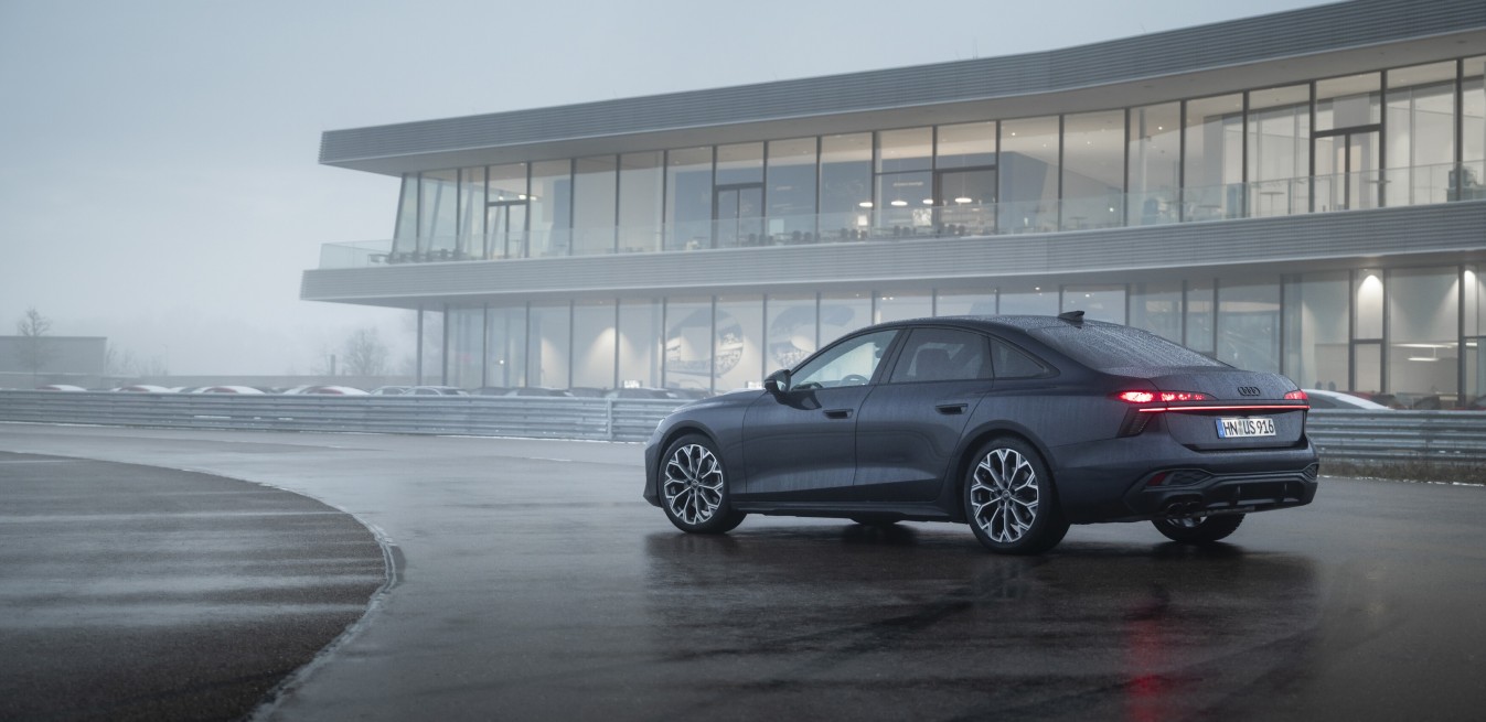 Audi con motor mhev sedán oscuro estacionado frente a edificio moderno con niebla