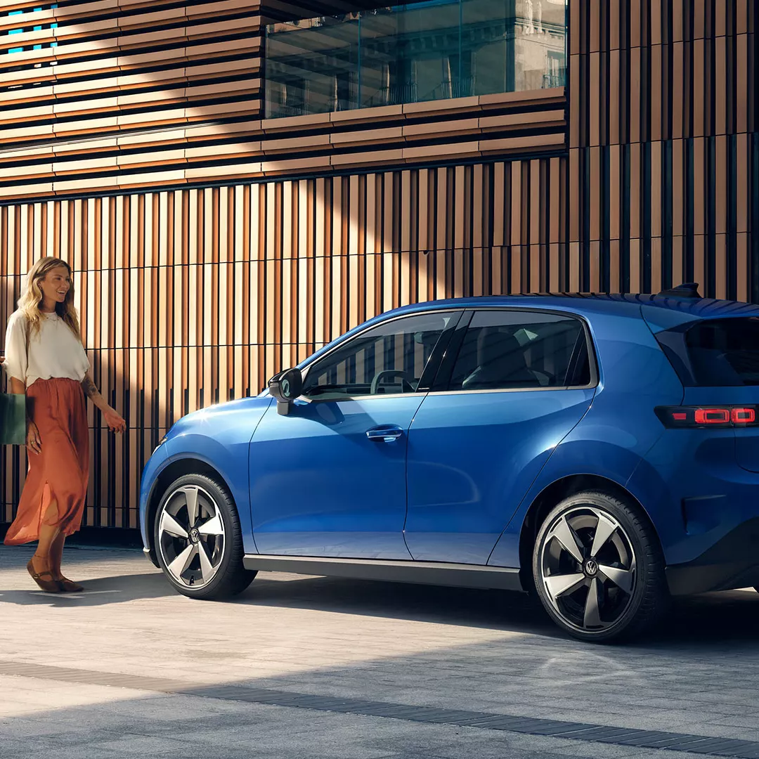 Mujer junto a Volkswagen ID.4 azul frente a fachada moderna