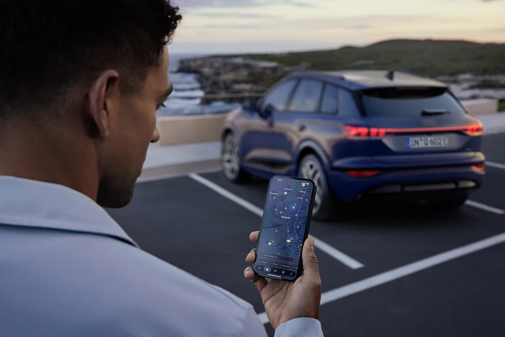 Hombre con smartphone controlando Audi Q6 e-tron en carretera con vistas al mar