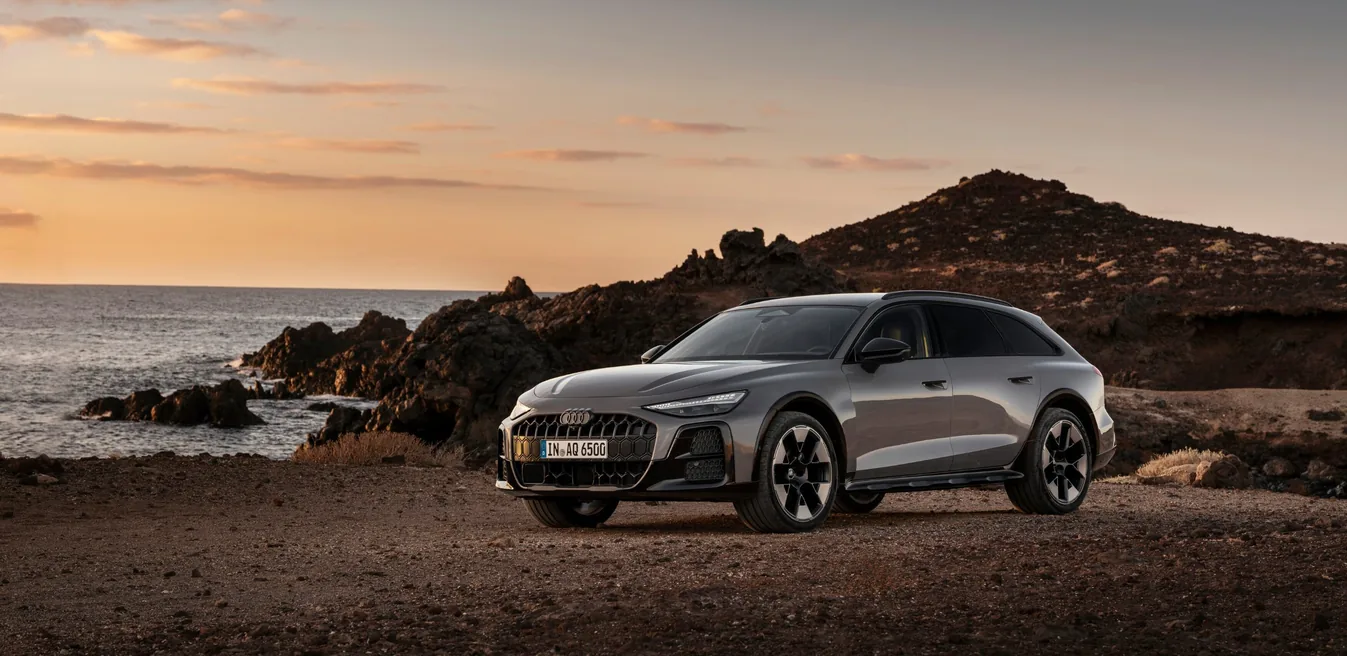Audi A6 allroad blanco estacionado en playa rocosa al atardecer