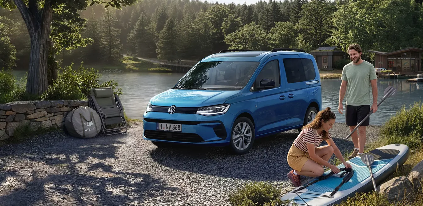 Volkswagen Caddy azul junto a un lago con familia disfrutando del ocio
