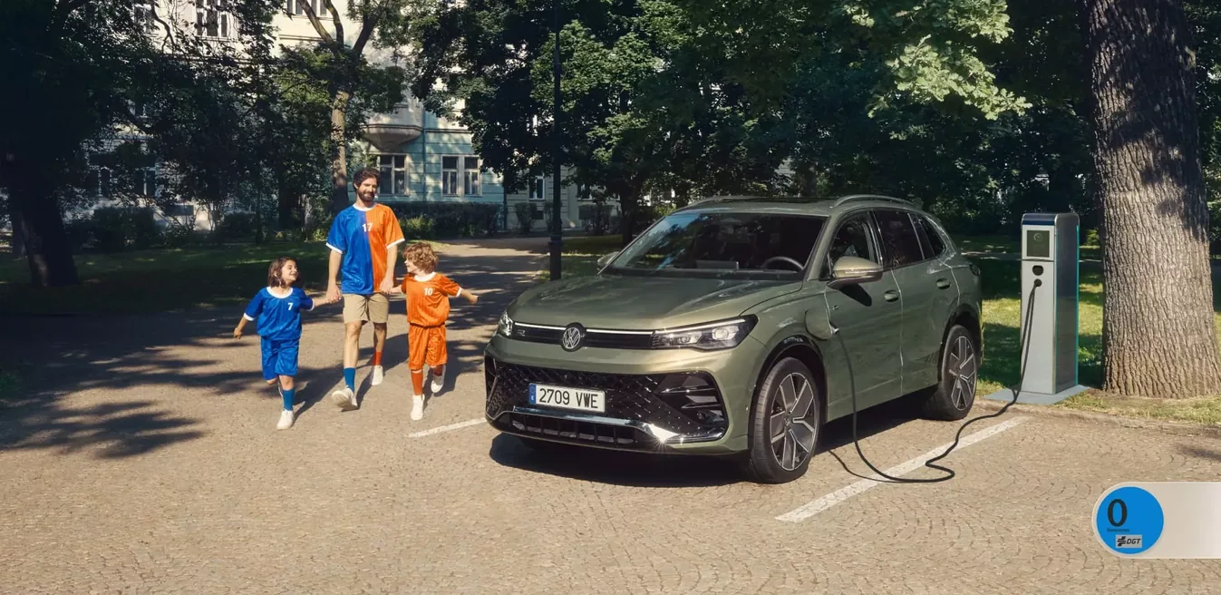 Volkswagen Tiguan eHybrid verde cargando en un punto de recarga junto a una familia, con el distintivo CERO de la DGT